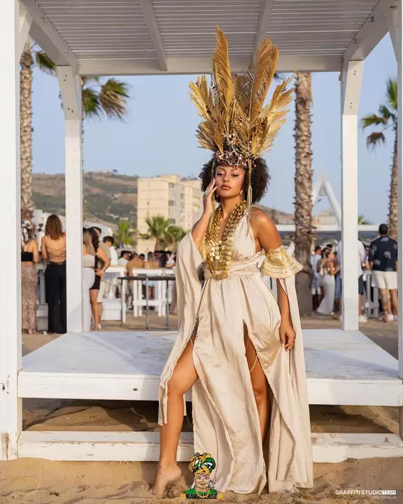 Performer in abito bianco e oro con copricapo di piume sulla spiaggia